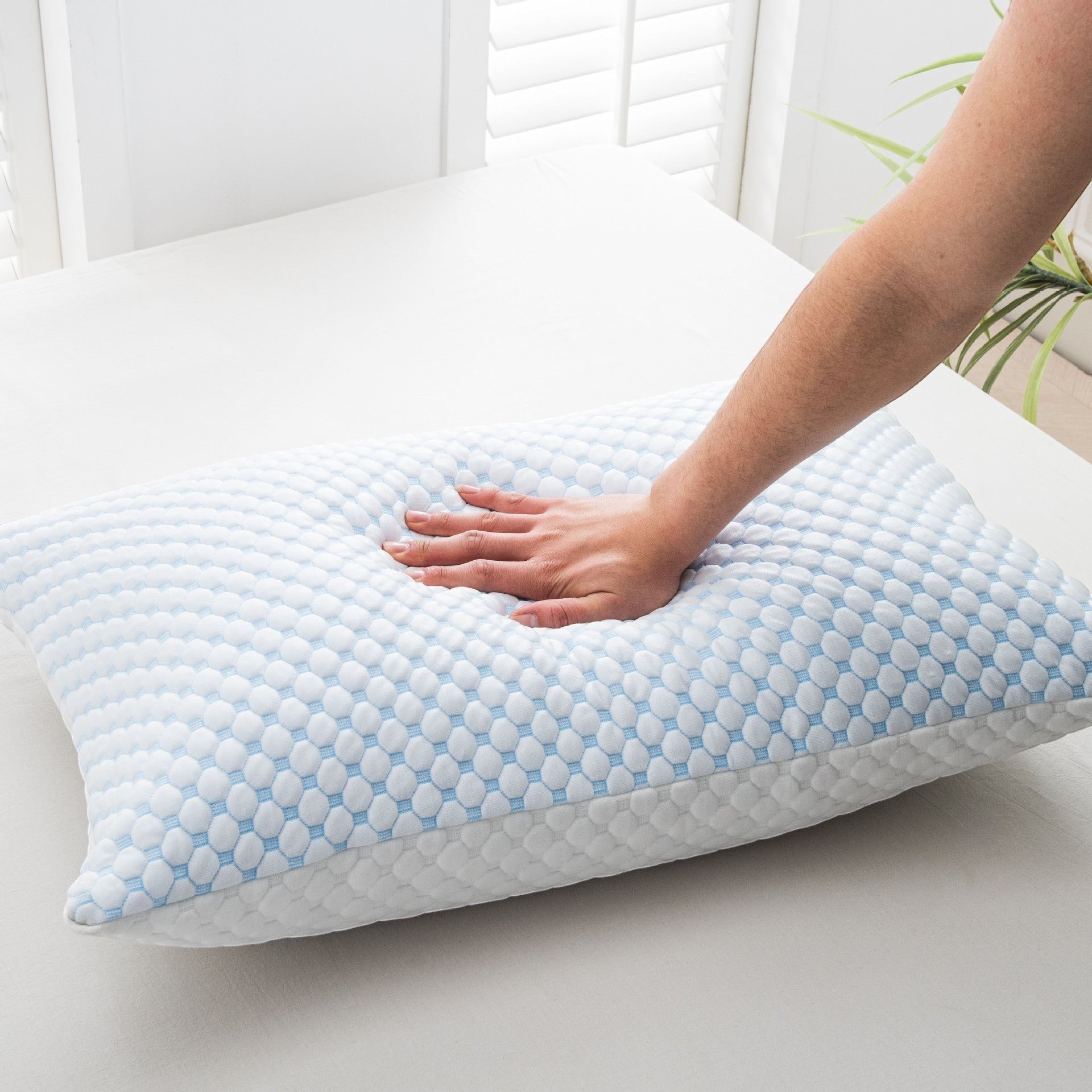 Hand pressing bamboo memory foam cooling pillow on bed
